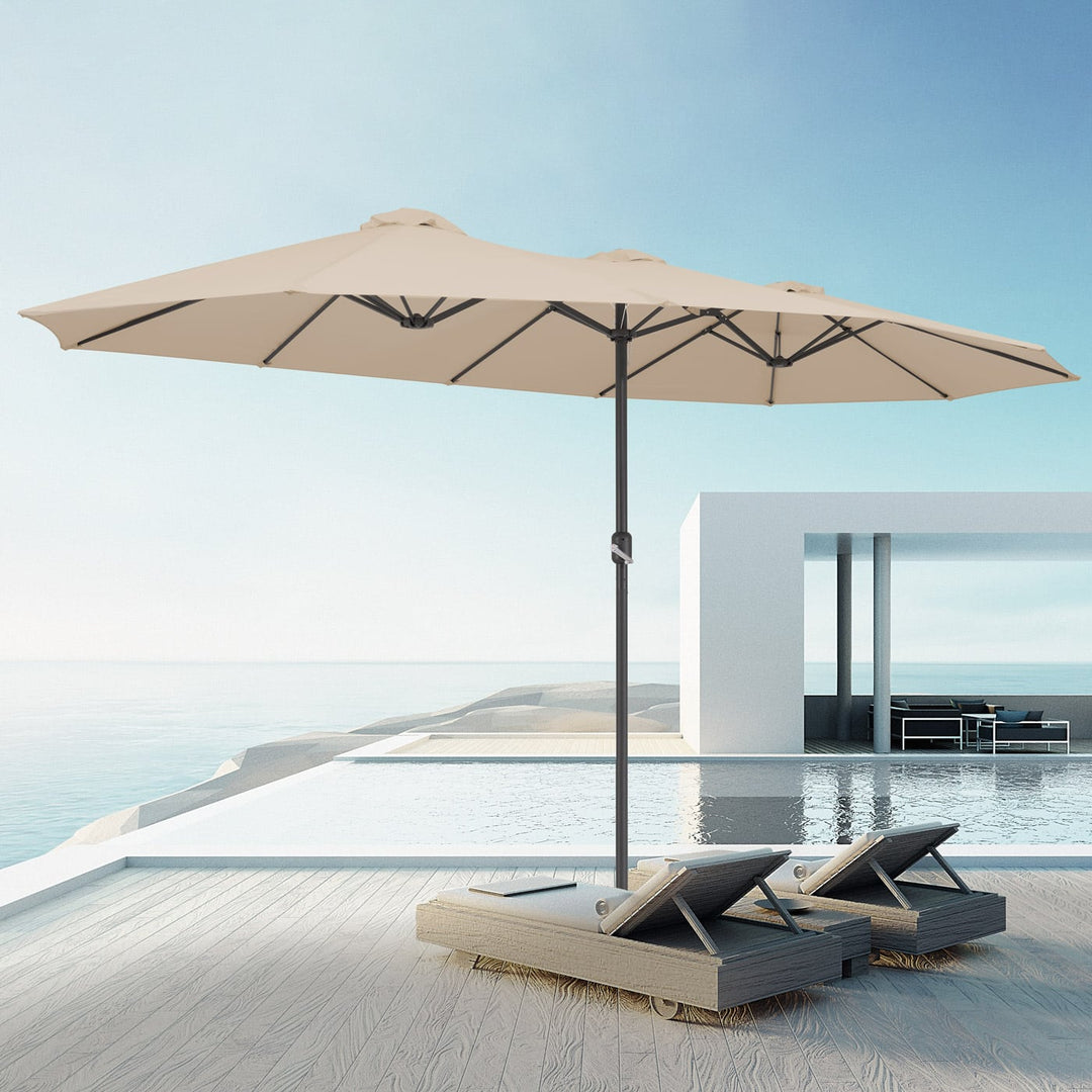 Stor lys dobbeltparasol der giver skygge over to liggestole på en terrasse ved en pool
