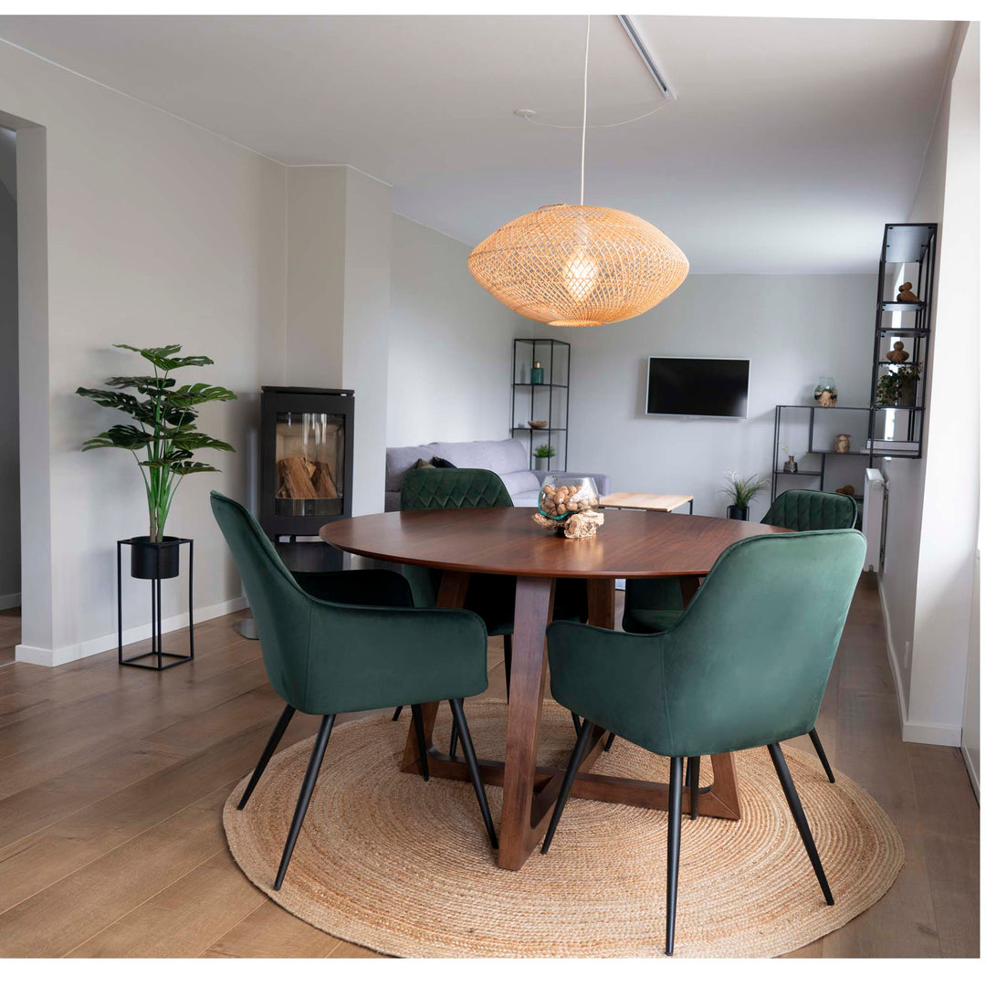 Rundt valnød-spisebord med grønne velour-stole på et rundt jutetæppe i en lys spisestue, et eksempel på korrekt størrelse og materiale på tæppe under spisebord
