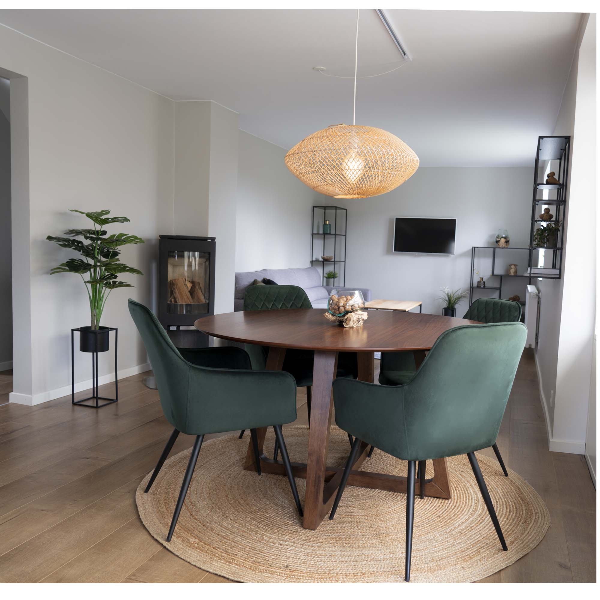 Rundt valnød-spisebord med grønne velour-stole på et rundt jutetæppe i en lys spisestue, et eksempel på korrekt størrelse og materiale på tæppe under spisebord