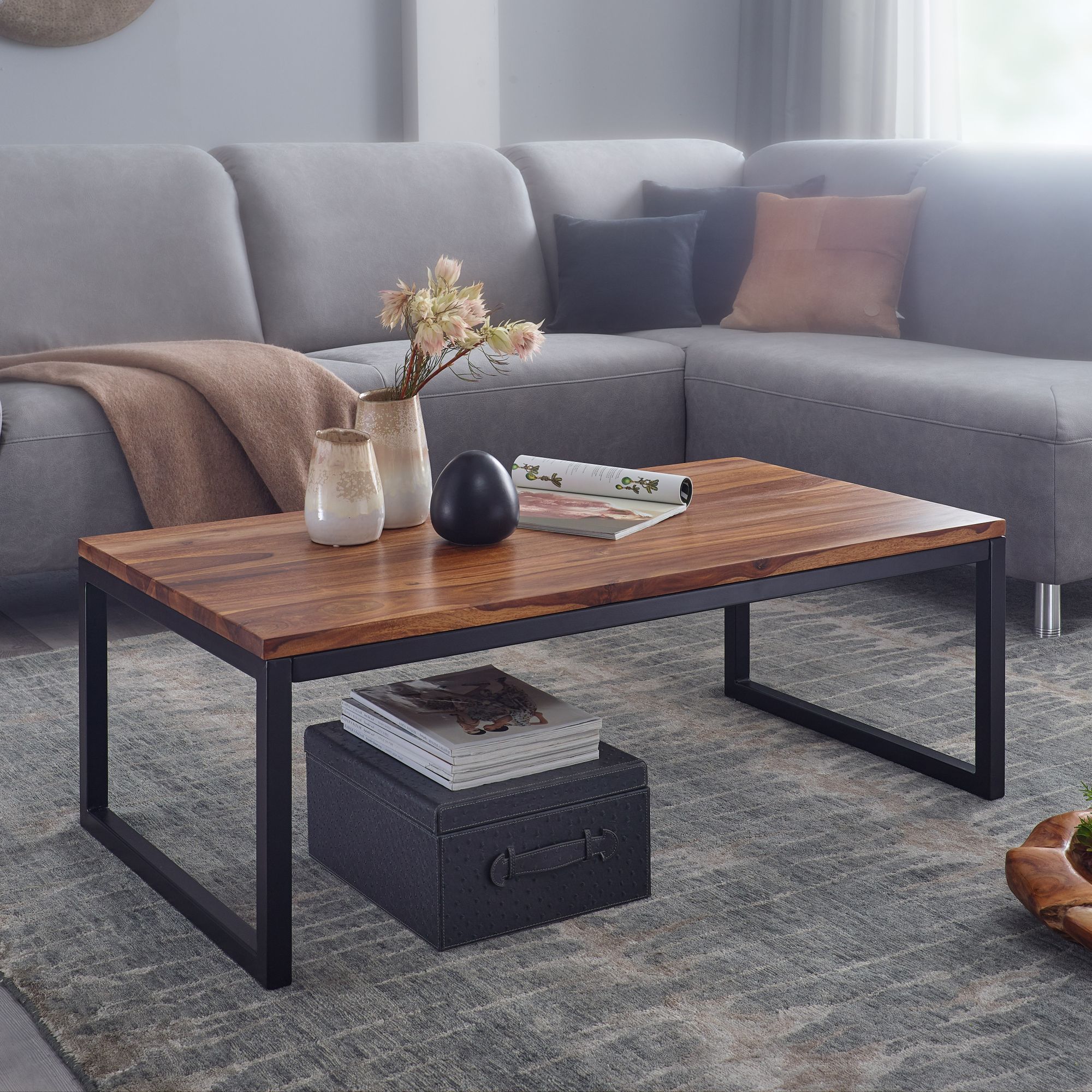 Industrielt sofabord i brun massivt træ med sort metal-stel placeret foran grå sofa med pude