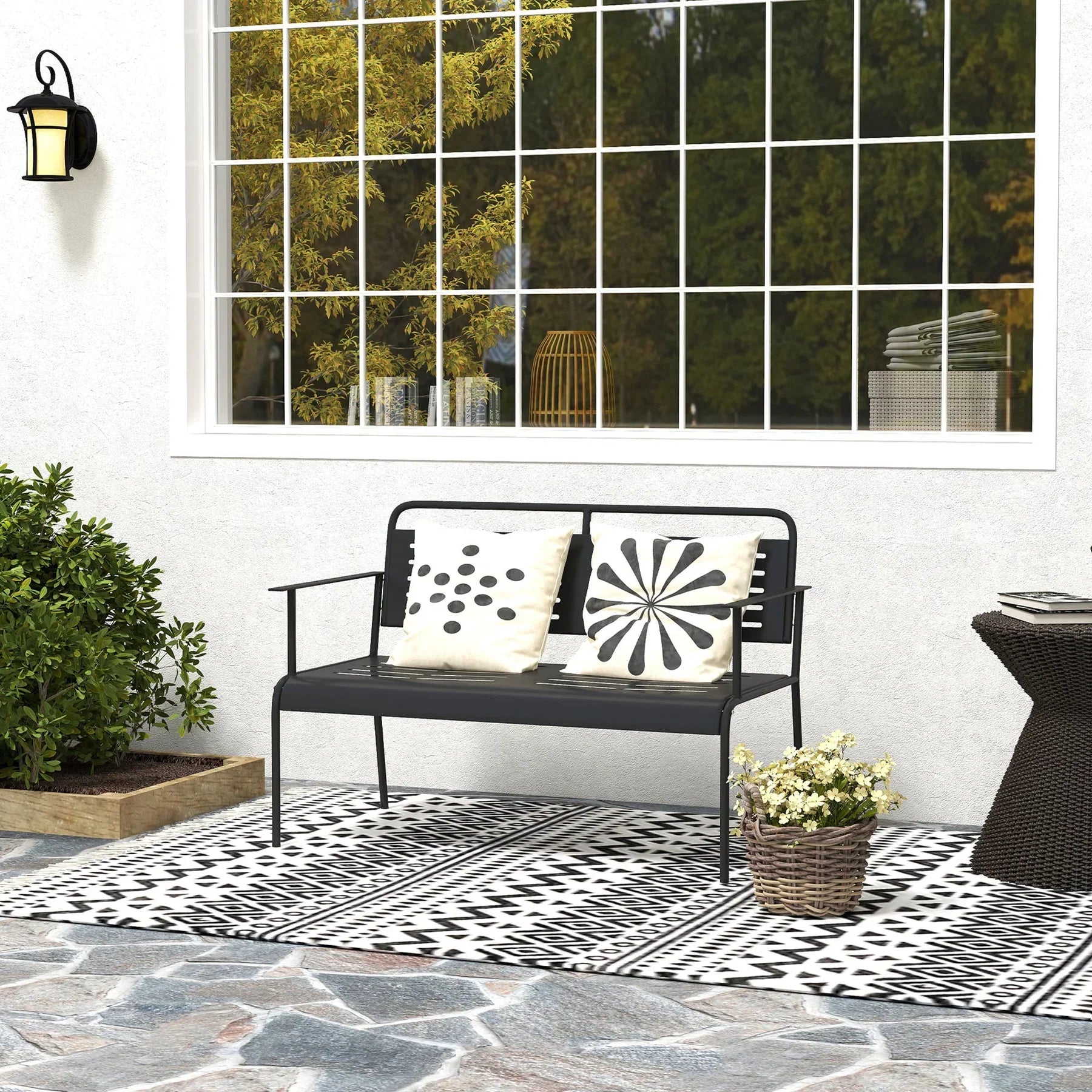 Sort metal havebænk på terrasse med pillows, taepper og potteplanter, lifestyle scene udendørs