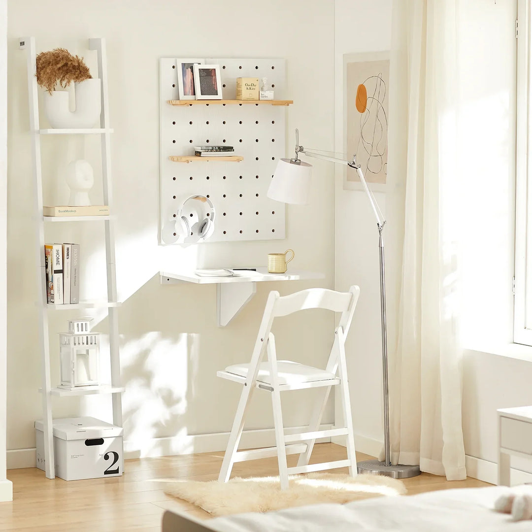 Hvidt vægmonteret klapbord i lyst rum med hvid stol pegboard og kunst i baggrunden