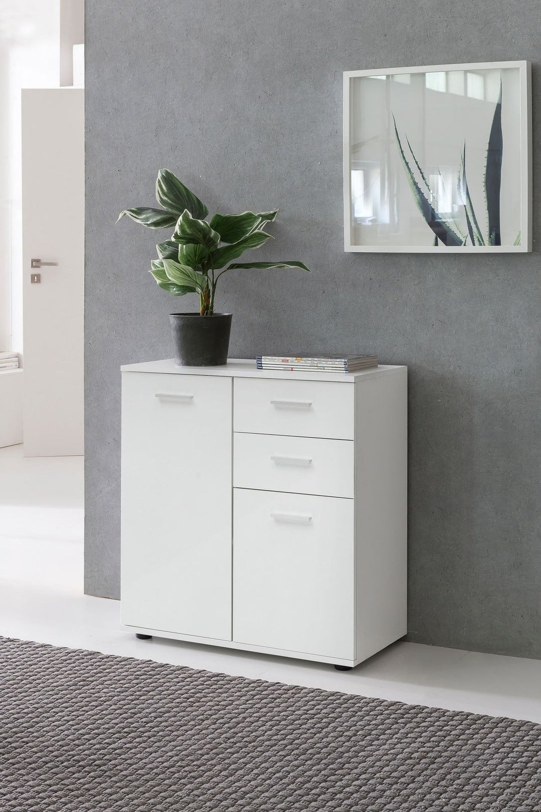 Hvid minimalistisk kommode med plante og spejl i en grå entré med groft tæppe