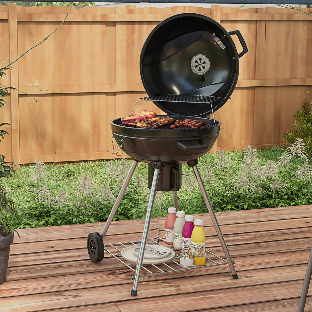 Sort kuglegrill med mad på grillristen i have med trælawn og blomster