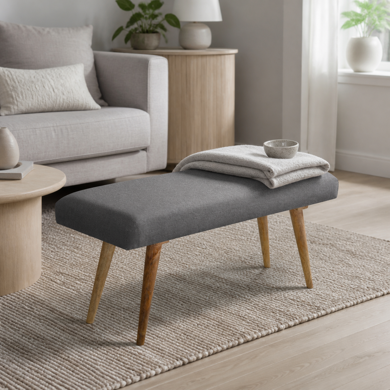 den grå polstrede bænk i lys grå stue med sofa, lyst træ, vævet uld og den polstrede bænk som materialemellemled
