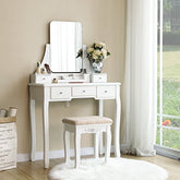 Hvidt toiletbord med rammeløst spejl og 5 skuffer samt en blomstervase placeret ved siden af vindueshjørnet