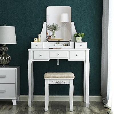 Hvidt toiletbord med rammeløst spejl og 5 skuffer samt en blomstervase placeret ved siden af sengebordet 