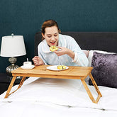 En kvinde med det sammenfoldelige bakkebord i bambusstil med justerbar hylde, der bruges til at lægge mad i sengen, mens hun spiser